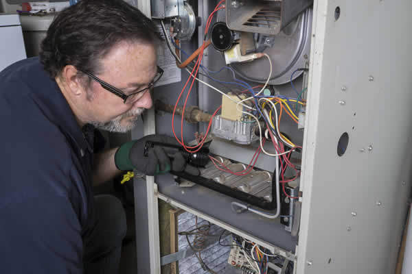 furnace technician with flashlight inspecting the inside of a furnace
