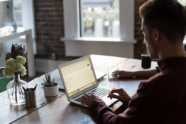 man sitting at table operating a laptop